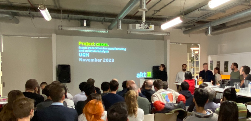 A group of people gathered before a presentation screen, before them are a seated audience watching the presentation. The screen details in text what is upcoming in the presentation.
