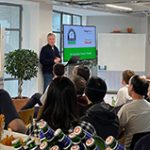 Photo of Paul Cowell, Director of Simply Rhino, standing in front of a group of seated people. Paul is introducing the upcoming Grasshopper UK User Meeting the opening slide of which is shown on two screens either side of him.