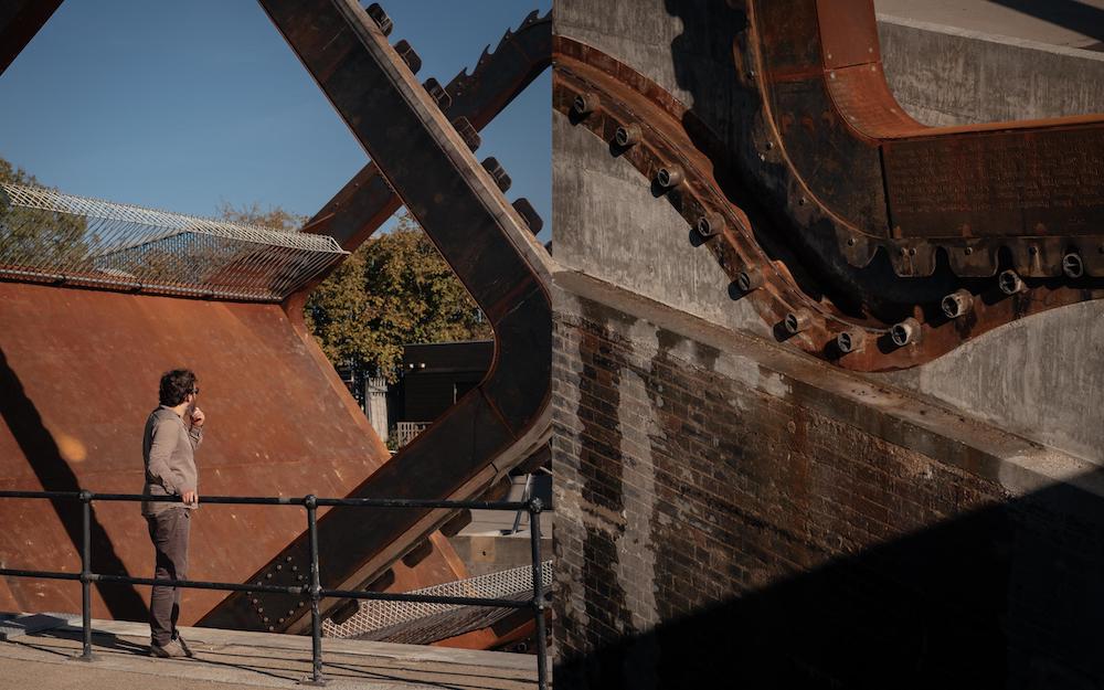 Photo shows a section of a rolling bridge with a man standing in the foreground looking at the bridge. The bridge is made from bricks and metal.